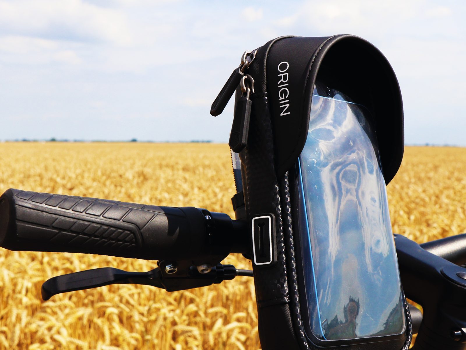 Waterdichte Origin-telefoonhouder op het stuur van een fiets, met een graanveld op de achtergrond